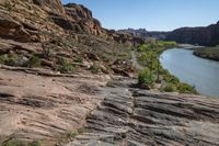 a mountain trail with rock formations above it and a river flowing through it in the foreground