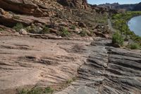 a mountain trail with rock formations above it and a river flowing through it in the foreground