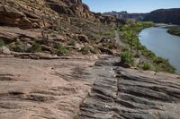 a mountain trail with rock formations above it and a river flowing through it in the foreground