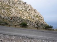a dirt and rocks road with a wooden bench in the middle of it and an ocean below