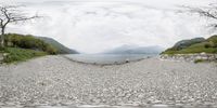 a paved road with some rocks near the lake and trees on the side of a mountain