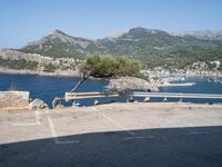 a bench in the middle of a parking lot next to some mountains and water near rocks and grass