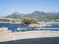 a bench in the middle of a parking lot next to some mountains and water near rocks and grass