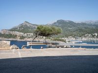 a bench in the middle of a parking lot next to some mountains and water near rocks and grass