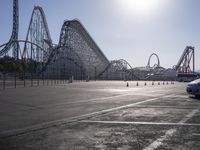 some parking lot with various roller coasters in background and two cars parked near them