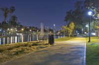 a path with benches and lights along it next to water, in the distance is a city at night