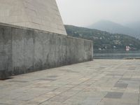 a long pathway in front of a concrete building with mountain views behind it in a city area