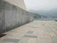 a long pathway in front of a concrete building with mountain views behind it in a city area