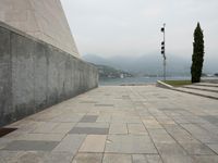 a long pathway in front of a concrete building with mountain views behind it in a city area