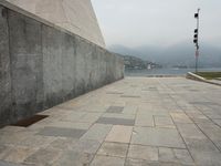 a long pathway in front of a concrete building with mountain views behind it in a city area