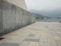 a long pathway in front of a concrete building with mountain views behind it in a city area