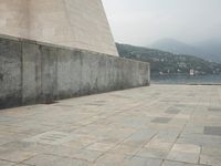 a long pathway in front of a concrete building with mountain views behind it in a city area