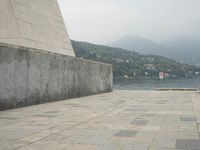 a long pathway in front of a concrete building with mountain views behind it in a city area