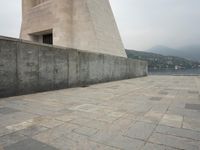 a long pathway in front of a concrete building with mountain views behind it in a city area