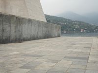 a long pathway in front of a concrete building with mountain views behind it in a city area