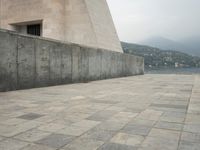 a long pathway in front of a concrete building with mountain views behind it in a city area