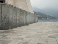 a long pathway in front of a concrete building with mountain views behind it in a city area