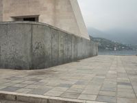a long pathway in front of a concrete building with mountain views behind it in a city area
