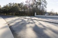 a paved road with white fences, grass and trees, and the sun is shining in the distance