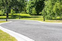 a paved country lane leads to a forested park and tree lined drive way, on the edge of a wooded area
