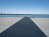 a pier with a long shadow casting a long line across it's water and bridge