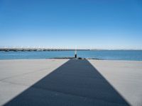 a pier with a long shadow casting a long line across it's water and bridge