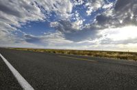 a paved street leads to the horizon of a prairie with clouds overhead and grass all around