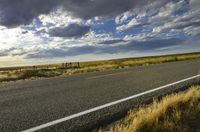 a paved street leads to the horizon of a prairie with clouds overhead and grass all around