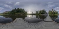 a wide fish - eye view of a river and land with trees surrounding it and a walkway along side the pond