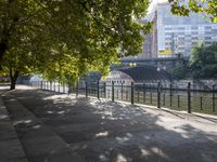 a scenic river path along an urban waterfront with buildings in the background and tree lined streets