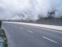 a road and a cliff on a cloudy day, with a steam - powered structure in the background