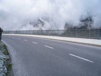 a road and a cliff on a cloudy day, with a steam - powered structure in the background