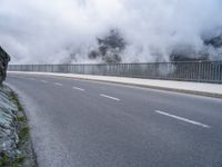 a road and a cliff on a cloudy day, with a steam - powered structure in the background