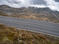 a person rides their bicycle along a winding road through mountains under cloudy skies and fluffy clouds