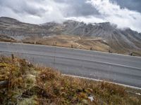 a person rides their bicycle along a winding road through mountains under cloudy skies and fluffy clouds