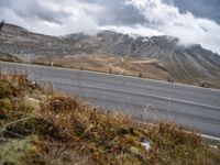 a person rides their bicycle along a winding road through mountains under cloudy skies and fluffy clouds