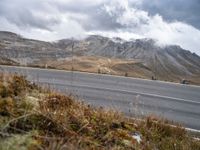 a person rides their bicycle along a winding road through mountains under cloudy skies and fluffy clouds