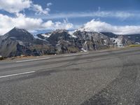 a road with white lines on it and mountains behind it in the distance, snow capped mountain range