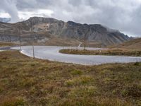 a view of the road to the mountains from behind it and below, with two poles, power lines, and grass