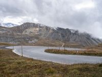 a view of the road to the mountains from behind it and below, with two poles, power lines, and grass