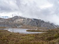 a view of the road to the mountains from behind it and below, with two poles, power lines, and grass