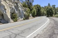 the road is paved and empty with some yellow markings on it in this area, along with rocks that point at the edge