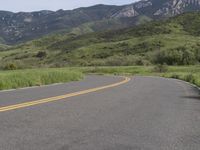 the bike is riding down the winding road between mountains, and a grassy valley in the background