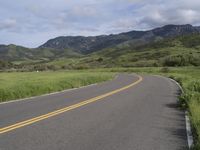 the bike is riding down the winding road between mountains, and a grassy valley in the background