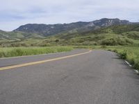 the bike is riding down the winding road between mountains, and a grassy valley in the background