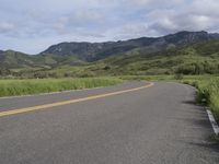 the bike is riding down the winding road between mountains, and a grassy valley in the background