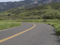 the bike is riding down the winding road between mountains, and a grassy valley in the background