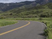 the bike is riding down the winding road between mountains, and a grassy valley in the background