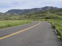 the bike is riding down the winding road between mountains, and a grassy valley in the background