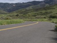 the bike is riding down the winding road between mountains, and a grassy valley in the background